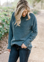 Blonde model wearing a ribbed teal sweater with a mocked neck.