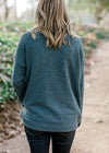 Back view of Blonde model wearing a teal sweater with a mocked neck.