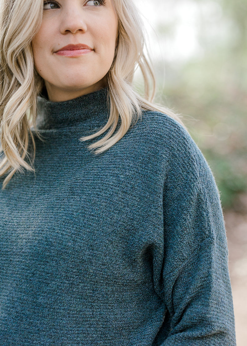 Close up view of Blonde model wearing a teal sweater. 