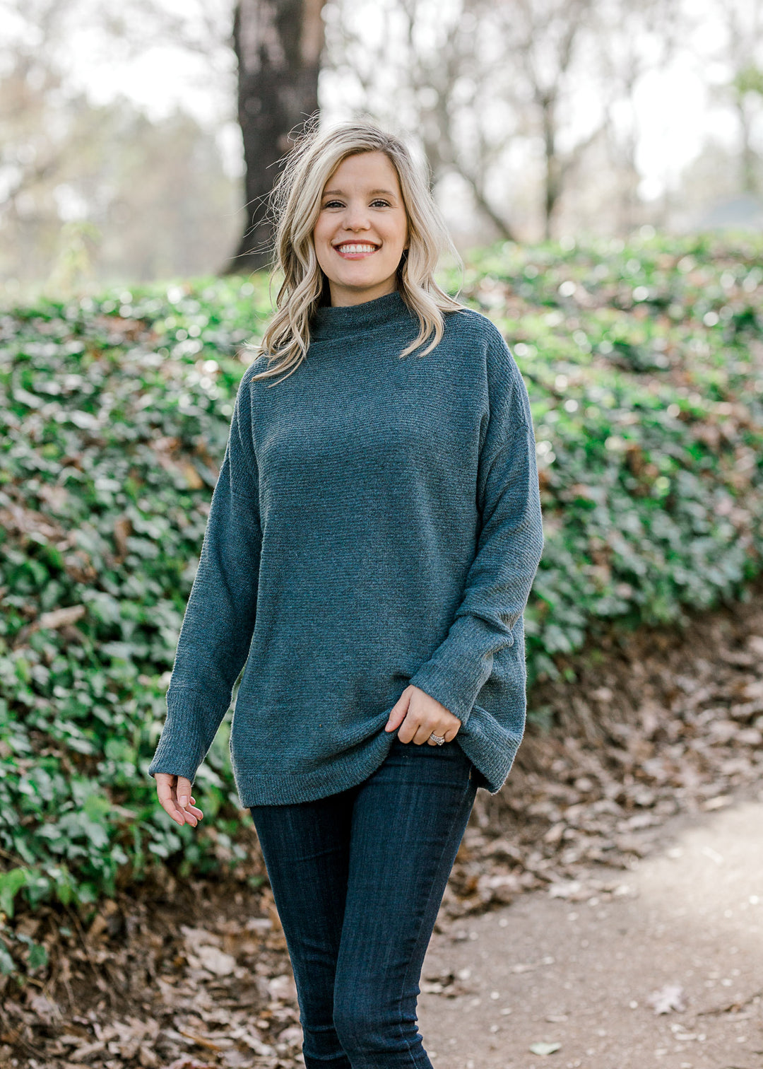 Blonde model wearing a teal sweater with jeans. 