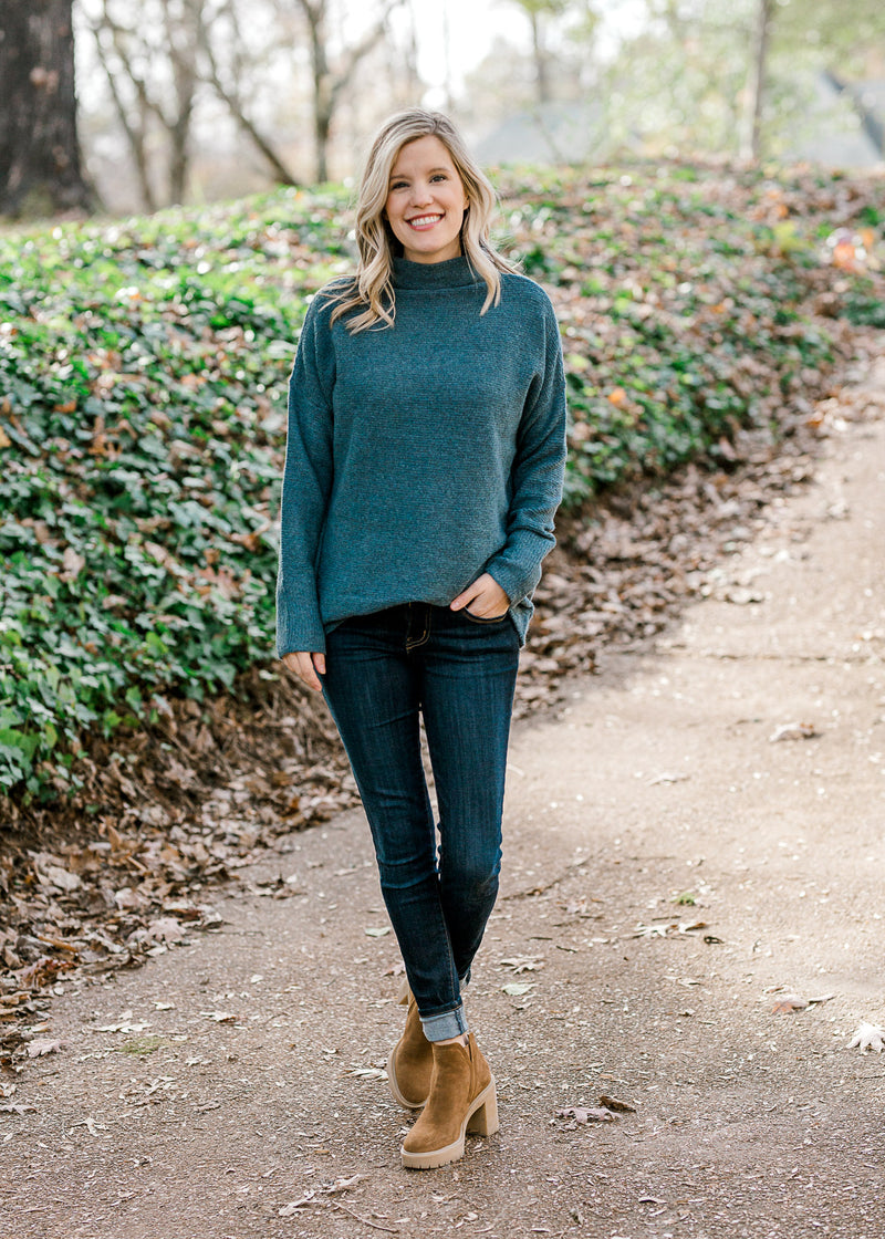 Blonde model wearing a teal sweater with jeans and booties. 