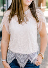 View of scalloped hem of Brunette model wearing cream colored cut lace top.