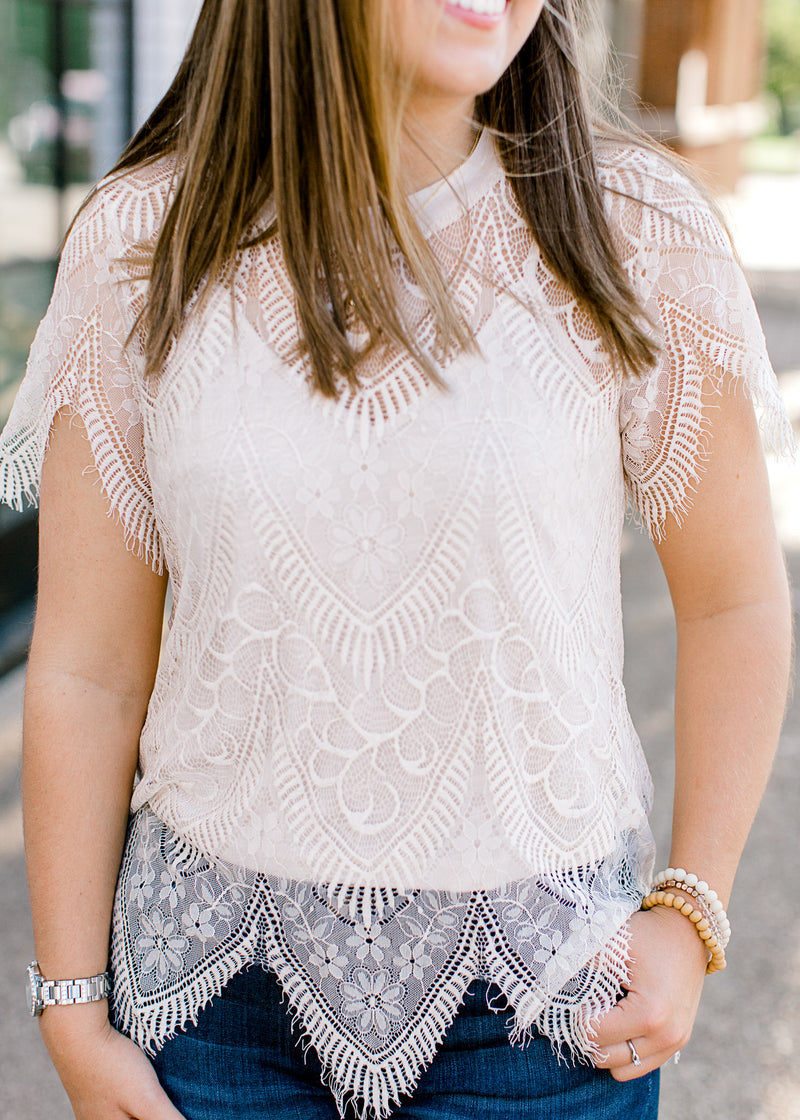 View of scalloped hem of Brunette model wearing cream colored cut lace top.