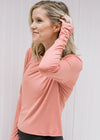 Blonde model wearing an apricot color long sleeve athletic top with black bottoms.
