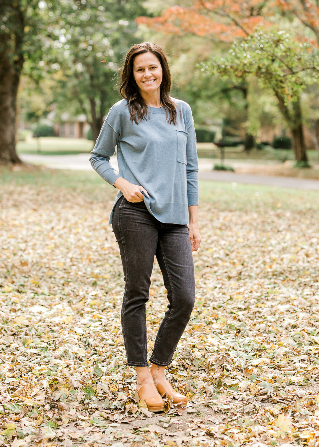 Brunette model wearing an ash blue sweater with black jeans.