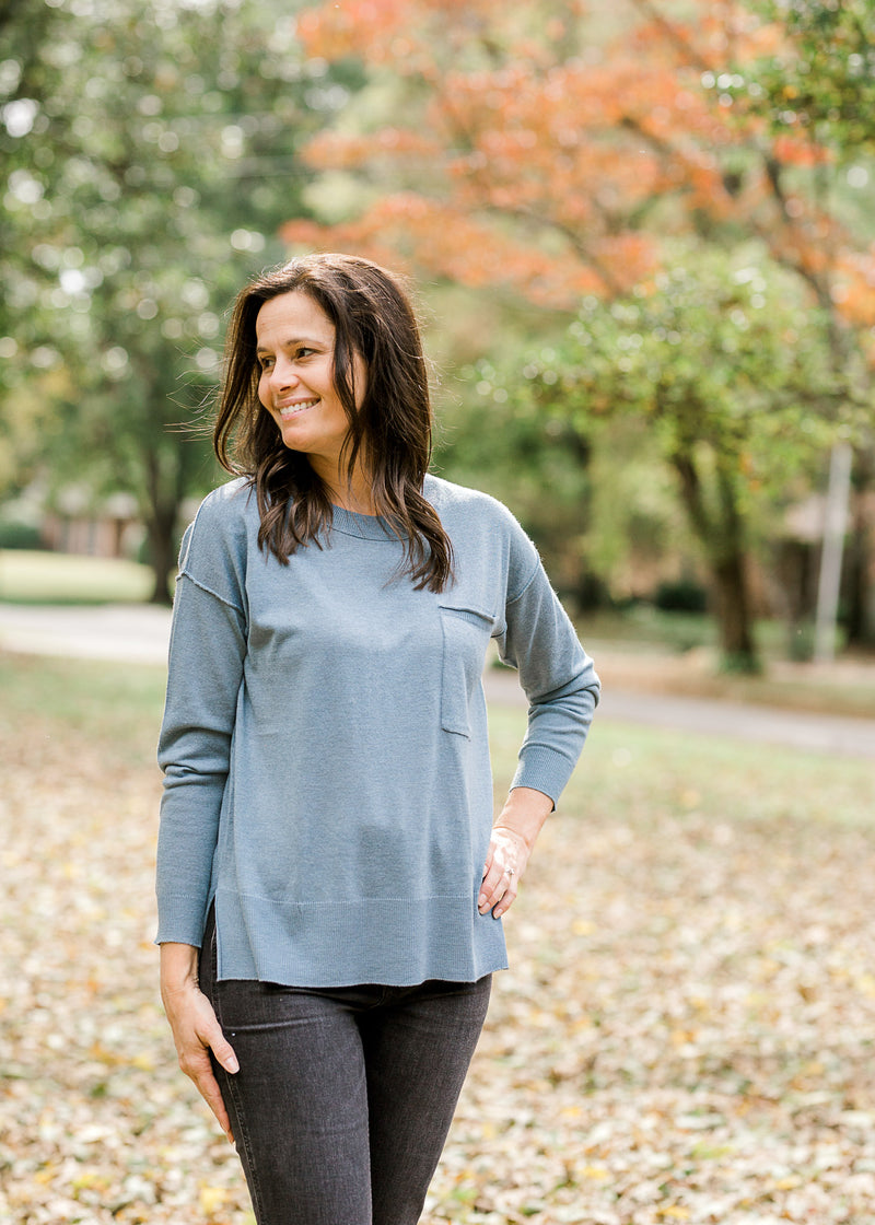 Brunette model looking to the side while wearing an ash blue sweater with black jeans.