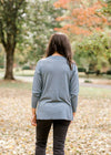 Back view of Brunette model wearing an ash blue sweater with black jeans.
