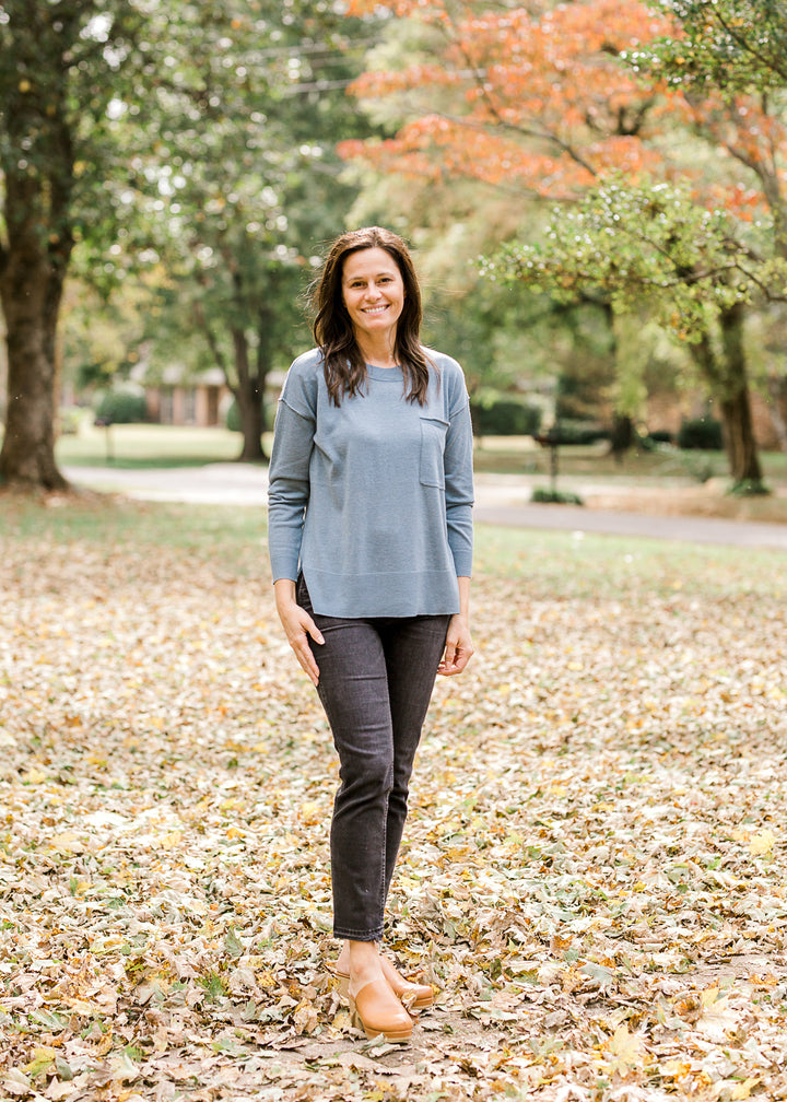 Brunette model wearing an ash blue sweater with black jeans and mules.