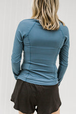 Back view of blonde model wearing blue, fitted athleisure top. 