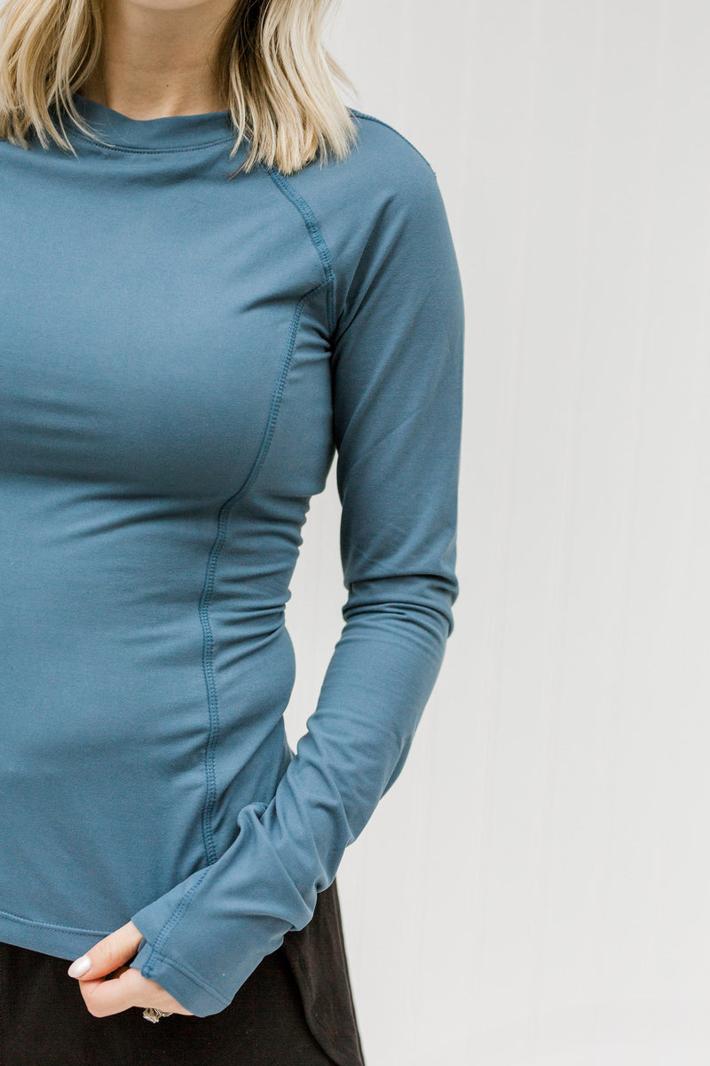 Close up view of blonde model wearing a fitted blue athleisure top with thumb hole.