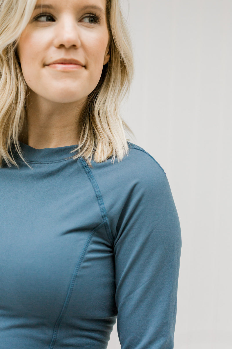 Close up view of blonde model wearing a fitted blue athleisure top.