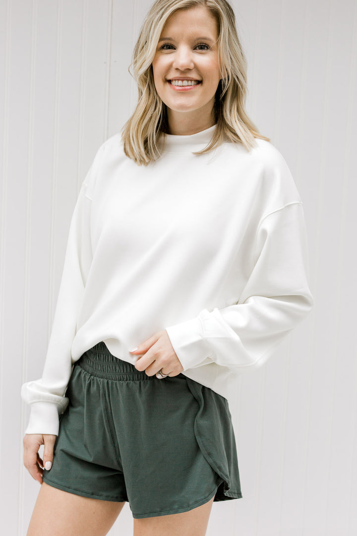Blonde model wearing a cream sweatshirt with hunter green shorts.