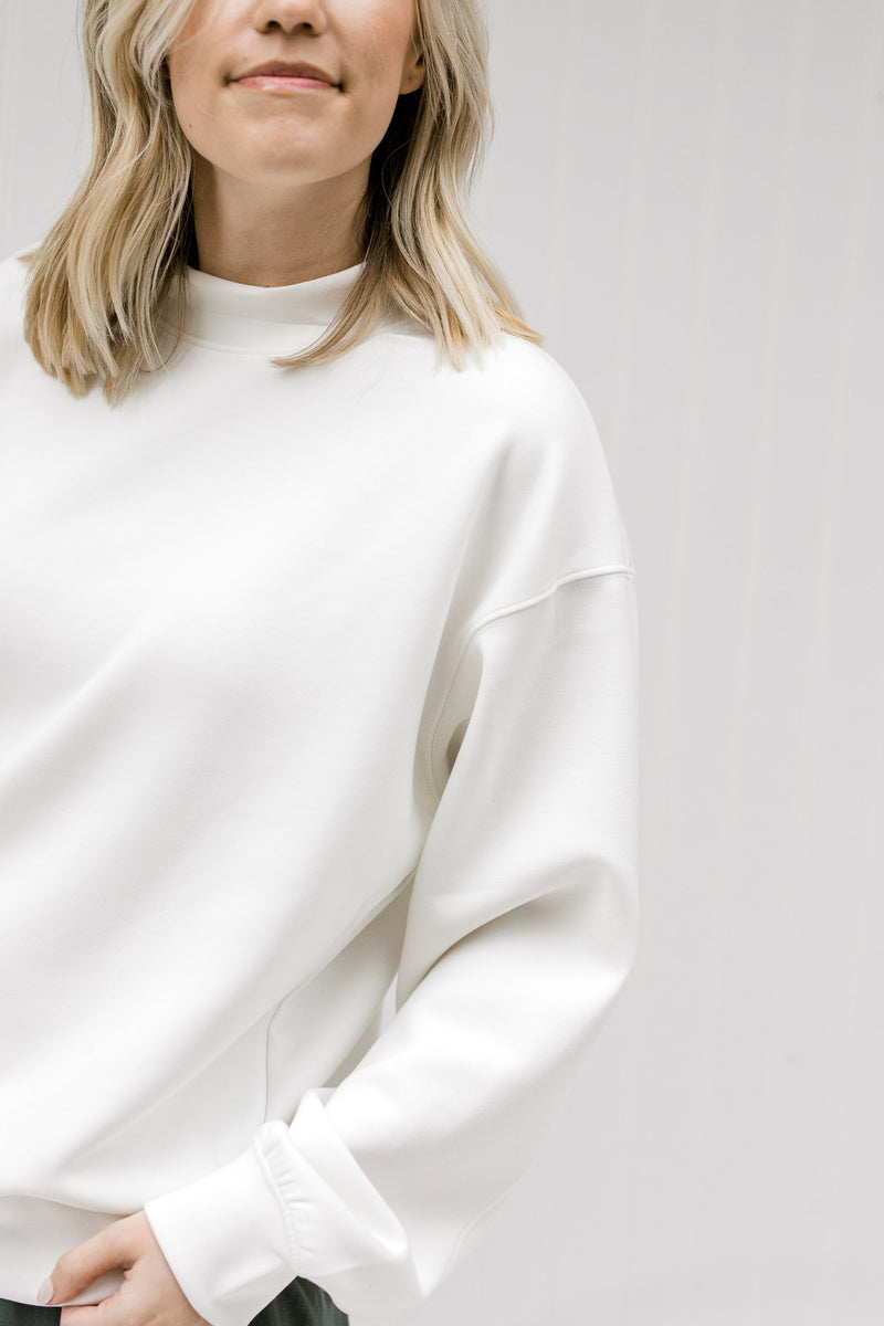 Close up view of Blonde model wearing a cream sweatshirt.