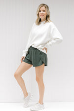 Blonde model wearing a cream sweatshirt with shorts and sneakers.