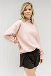 Blonde model wearing a pink sweatshirt with a mock neck.