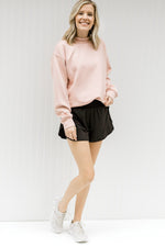 Blonde model wearing a pink sweatshirt with black shorts and tennis shoes.