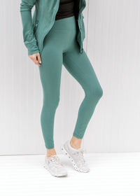 Model wearing teal leggings with black top and a jacket. 