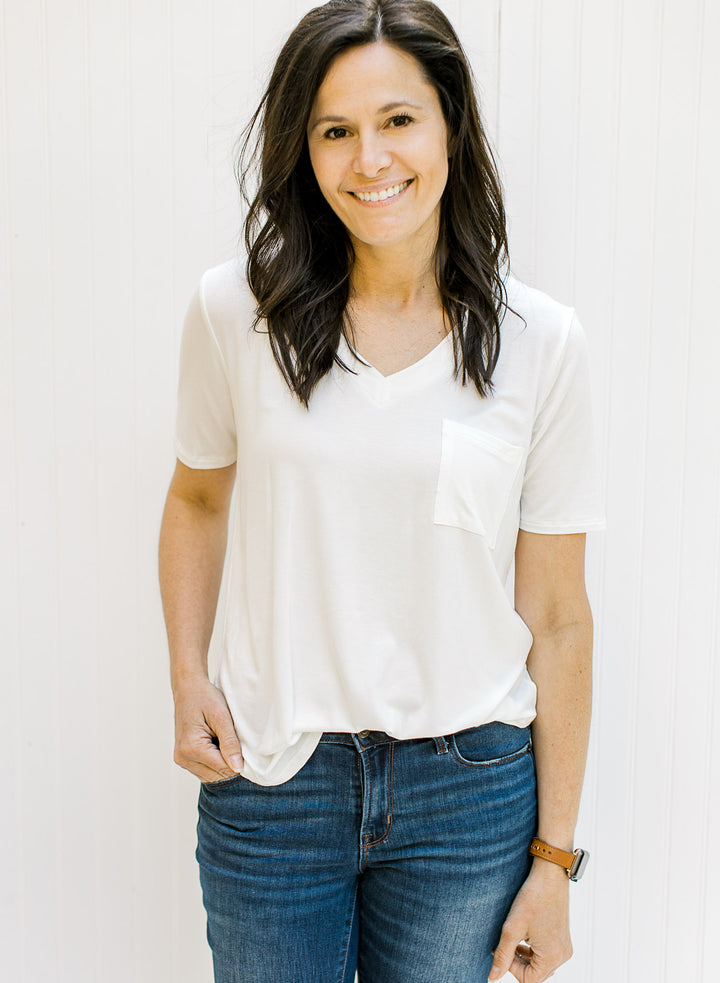 Model wearing a ivory colored short sleeve v-neck tee with a chest pocket. 