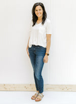 Model wearing a ivory colored short sleeve v-neck tee with a chest pocket with jeans and sandals. 