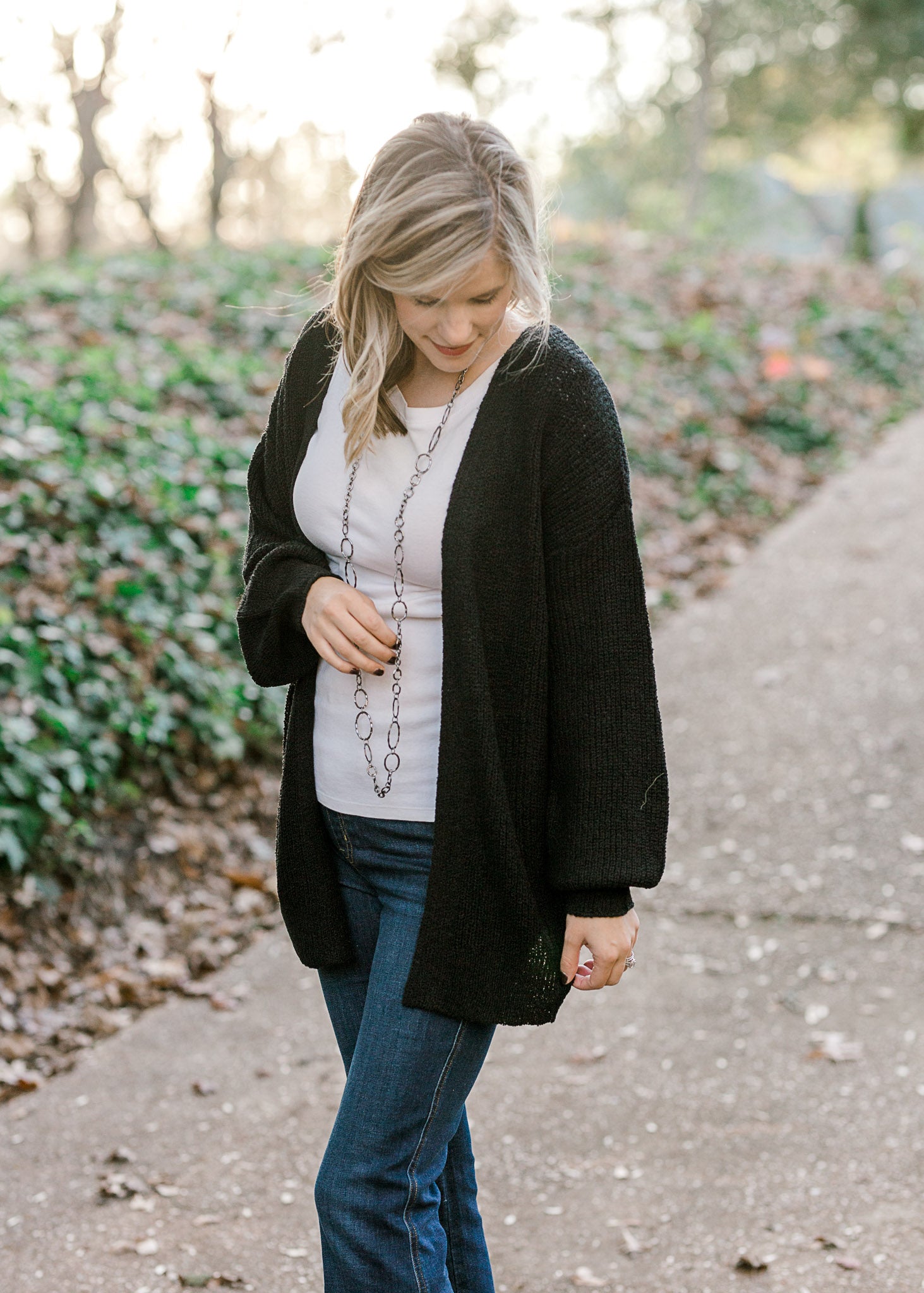 Blonde model wearing black cardigan with white top and jeans. 