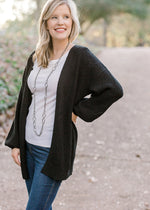 Blonde model wearing black cardigan with white top, jeans and a silver necklace. 
