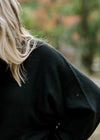 Close up view of sleeve on blonde model wearing a black sweater. 