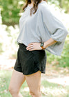 Brunette model wearing black elastic waist tulip shorts and loose shirt.