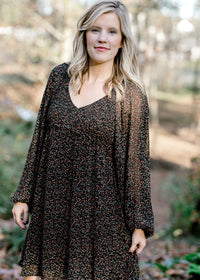 Blonde model wearing black, v-neck dress with ditsy pink floral pattern. 