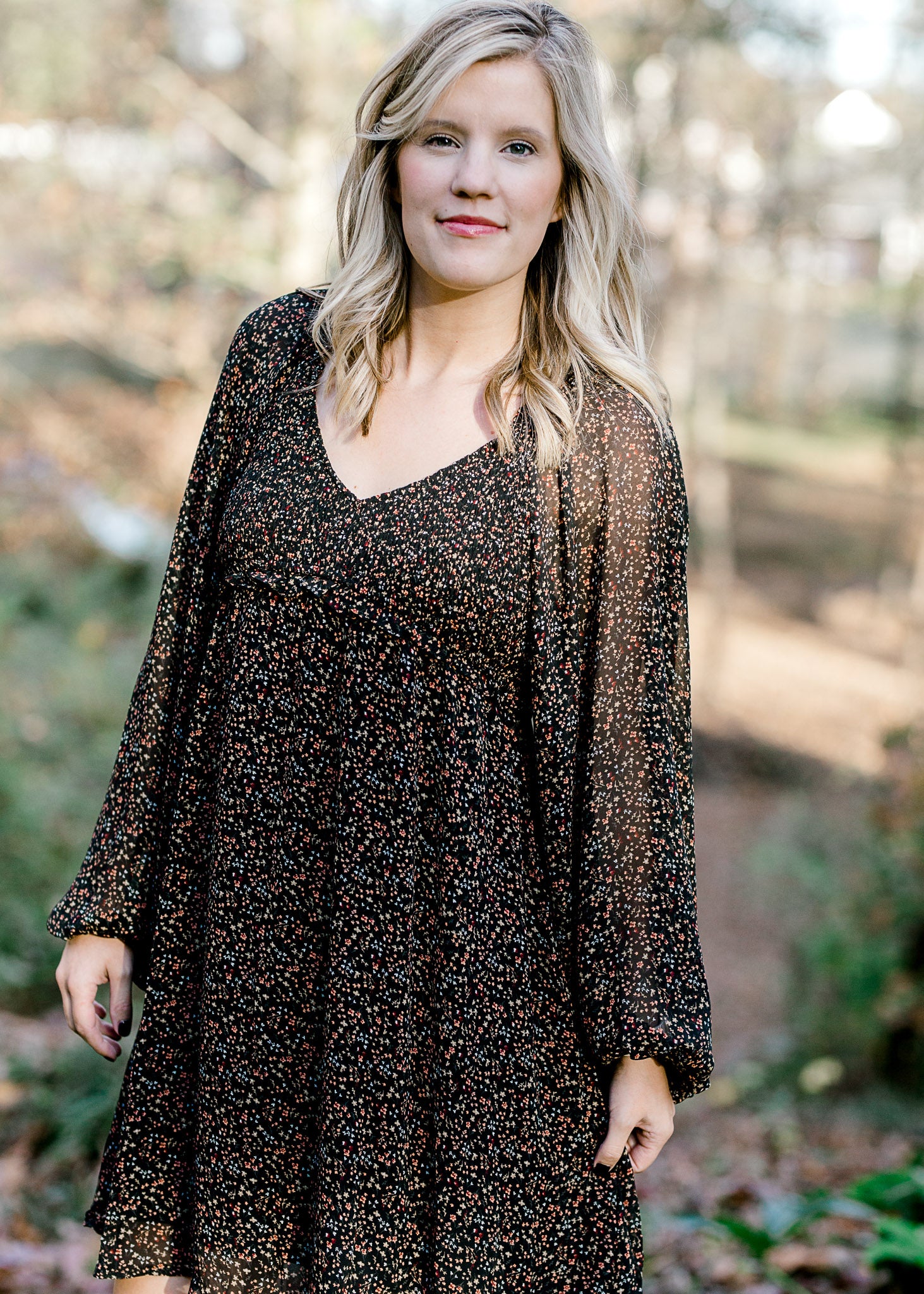 Blonde model wearing black, v-neck dress with ditsy pink floral pattern. 