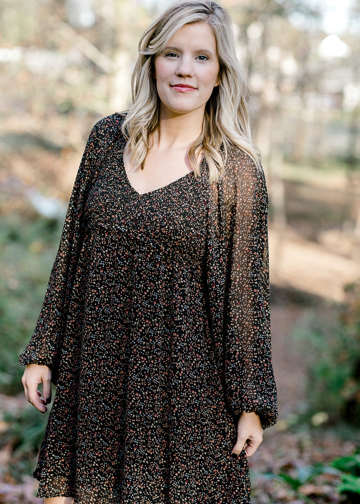 Blonde model wearing black, v-neck dress with ditsy pink floral pattern. 