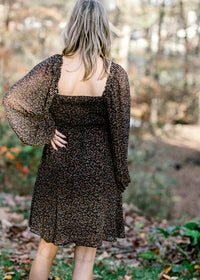 Back view of square neckline on Blonde model wearing black dress with ditsy pink floral pattern. 