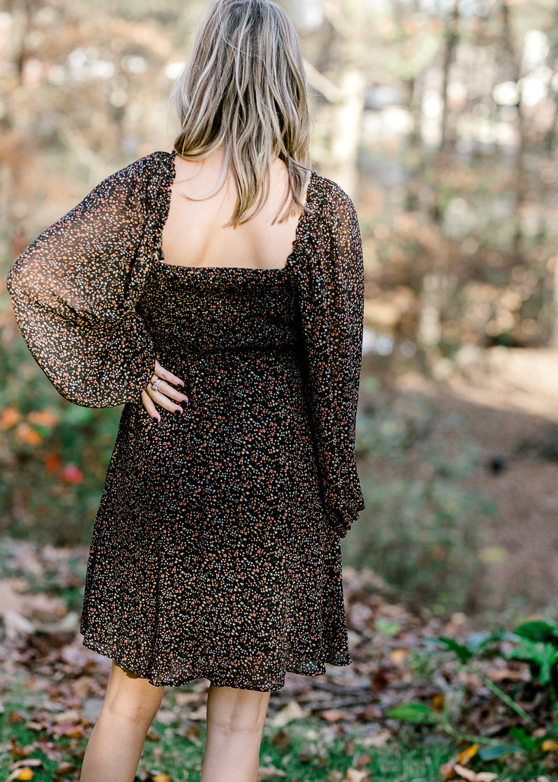 Back view of square neckline on Blonde model wearing black dress with ditsy pink floral pattern. 