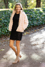 Blonde model wearing black sequin dress and faux fur jacket.