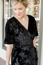 Neckline view of Blonde mode wearing floral tone on tone black velvet dress.