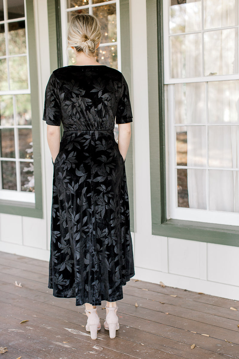 Back view of Blonde mode wearing floral tone on tone black velvet dress.