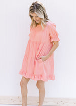 Model wearing a pink above the knee dress with bubble short sleeves and a flowy tiered design. 