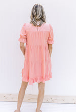 Back view of Model wearing a pink dress with bubble short sleeves and a flowy tiered design. 