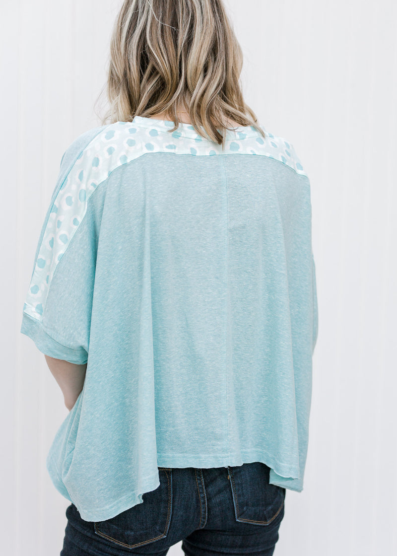 Back view of blonde model wearing a light blue top with blue pattern along shoulders. 