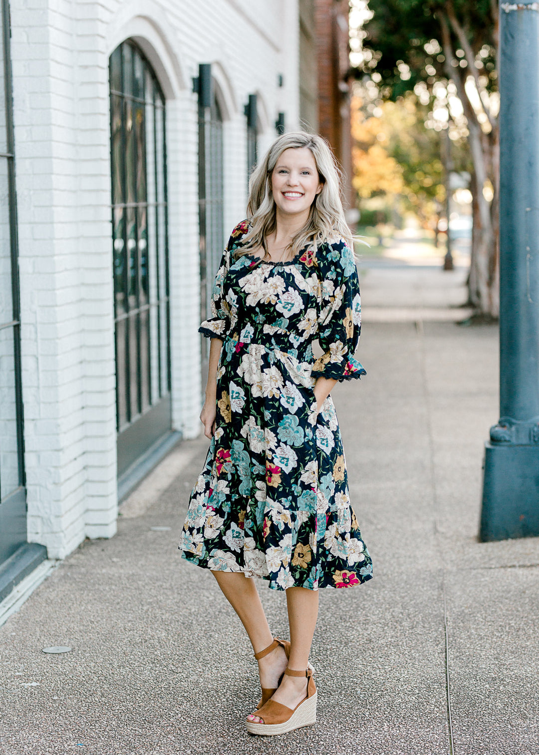 Blonde model wearing navy midi dress with floral pattern. 