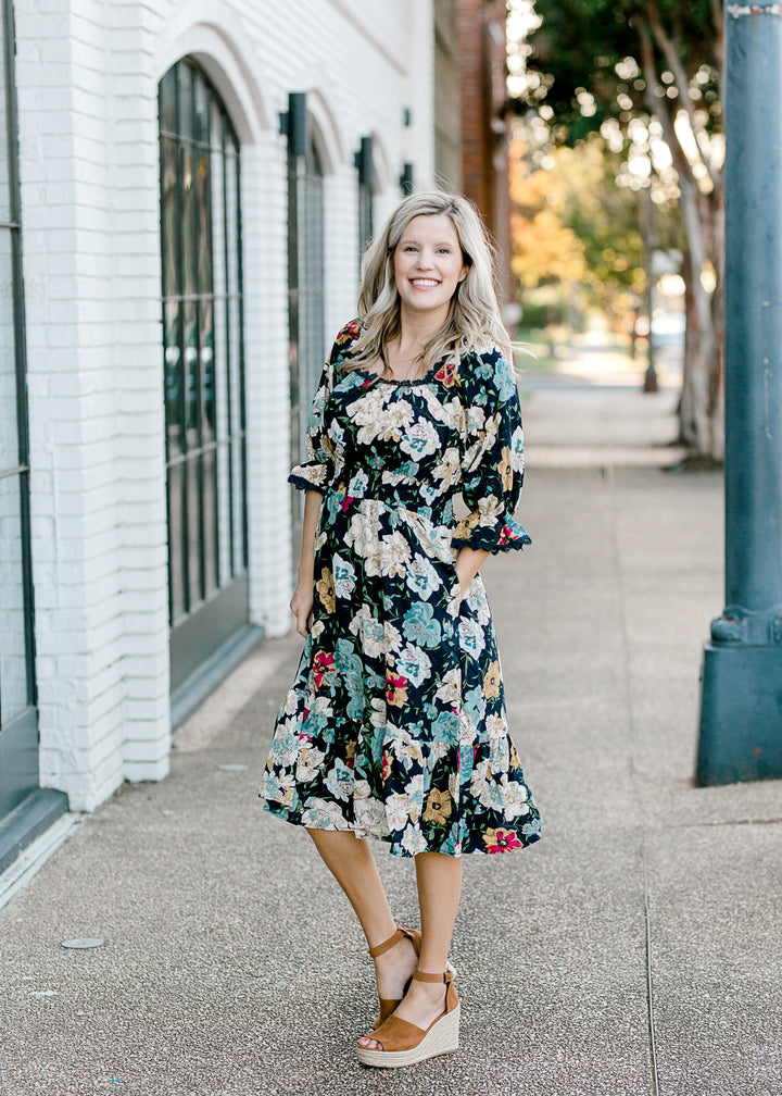 Blonde model wearing navy midi dress with floral pattern. 