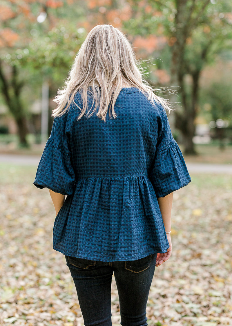 Back view of Blonde model wearing navy checked button up top.