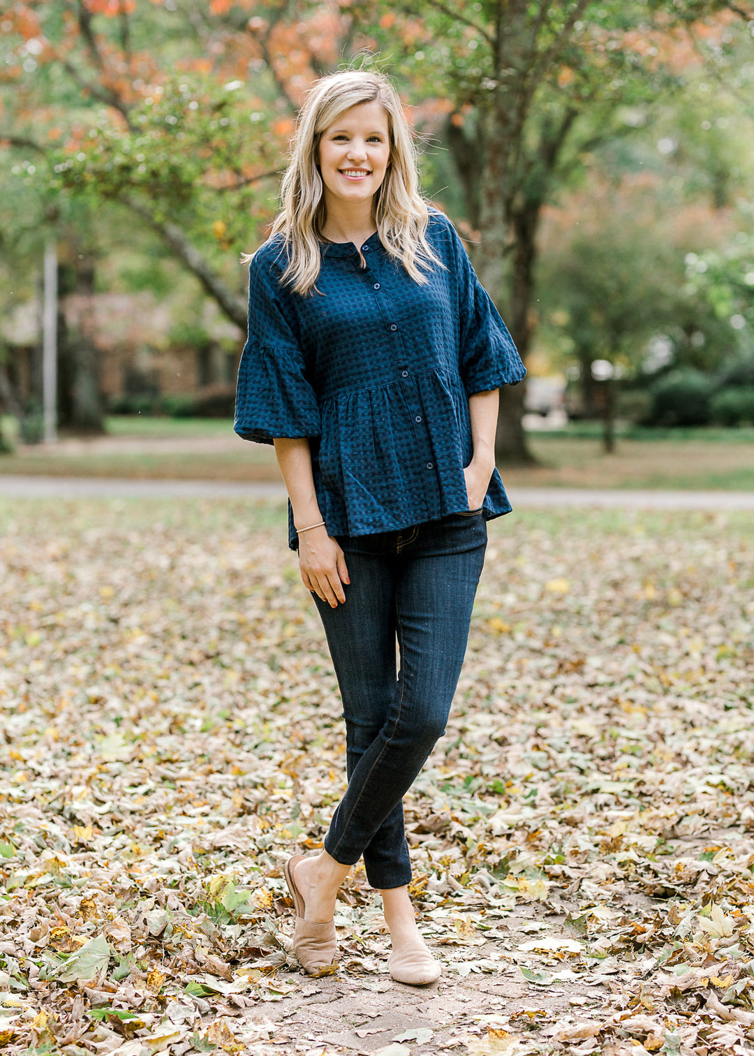 Blonde model wearing navy checked button up top with jeans and flat mules.