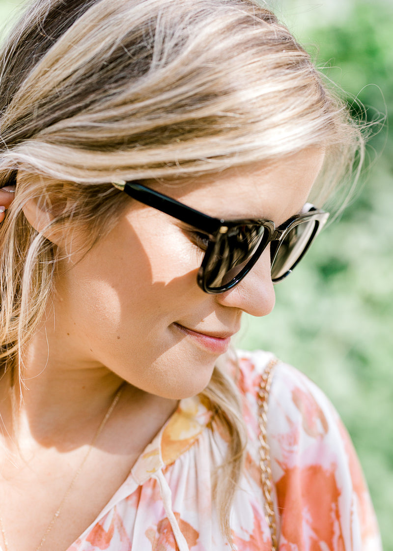 Blonde model wearing black sunglasses with gold accents.