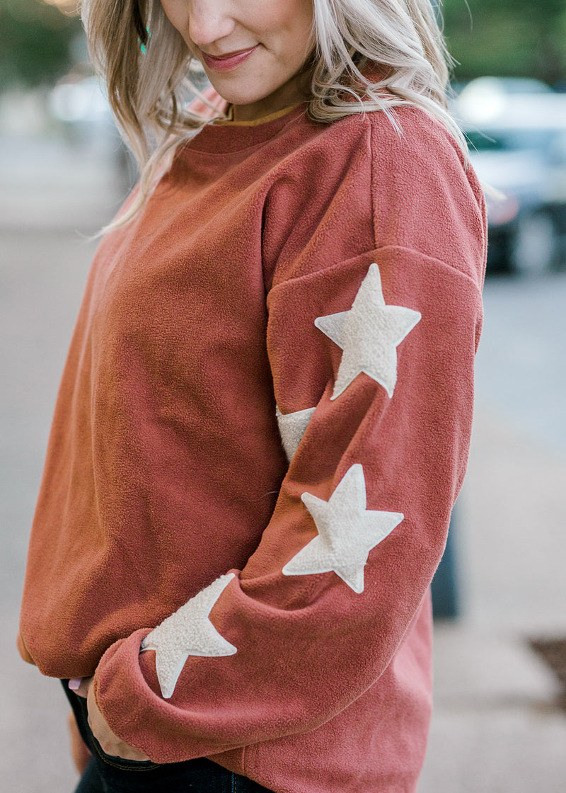Close up of star detail on the sleeve of a mauve sweater. 