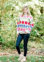 Blonde model wearing cream sweater with bright floral pattern with jeans and booties.