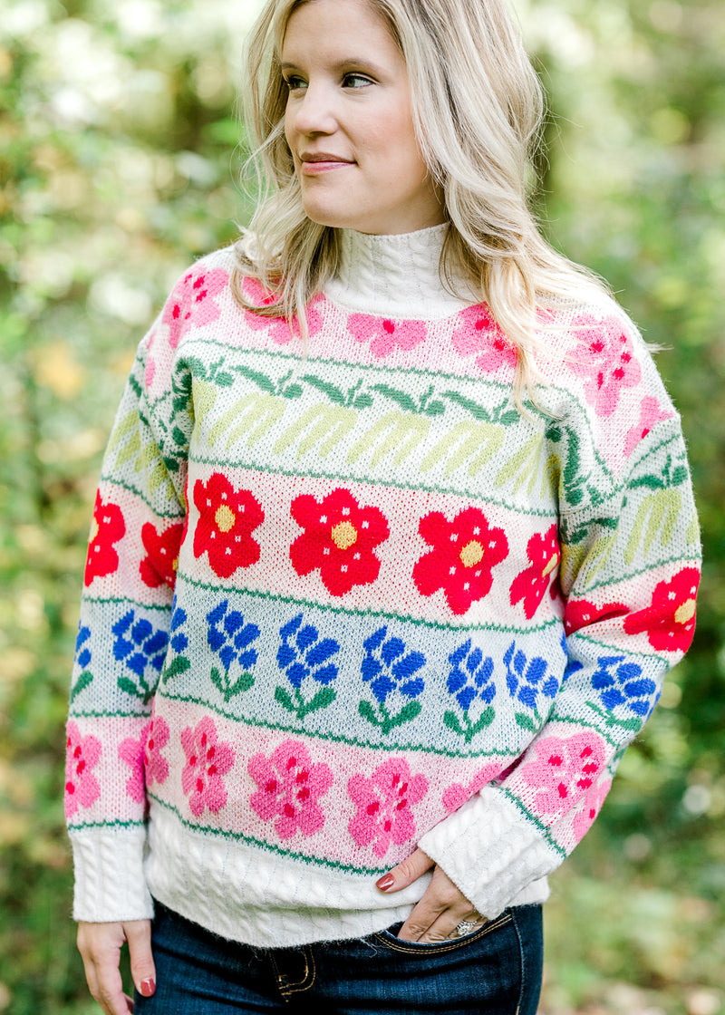 Blonde model wearing cream sweater with bright floral pattern.