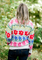 Back view of Blonde model wearing cream sweater with bright floral pattern.