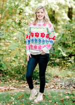 Blonde model wearing cream sweater with bright floral pattern and jeans.