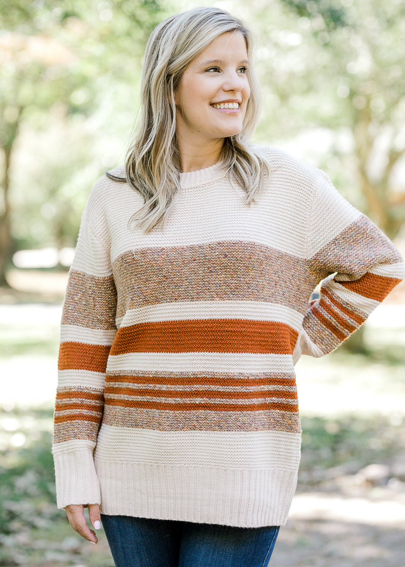 Blonde model wearing cream sweater with brown and rust stripes.