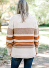 Back view of Blonde model wearing cream sweater with brown and rust stripes.